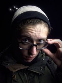 Close-up portrait of man wearing eyeglasses against black background