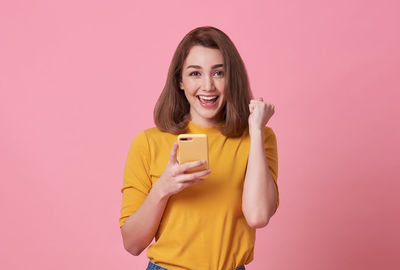 Portrait of smiling young woman standing against pink background