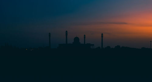 Silhouette factory against sky during sunset