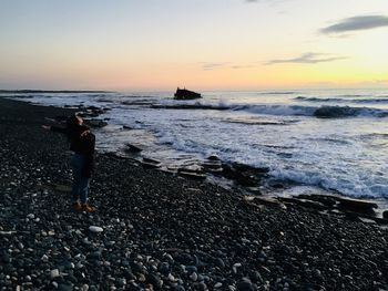 Woman with arms outstretched standing at beach during sunset