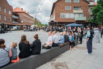 People sitting in town square against sky in city