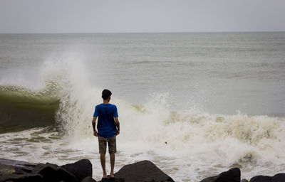 Rear view of man standing at beach against clear sky
