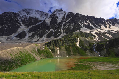 Scenic view of lake and snow covered mountains against cloudy sky