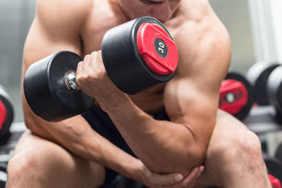 Shirtless muscular man exercising with dumbbells in gym