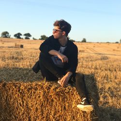 Portrait of young man sitting on hay against clear sky