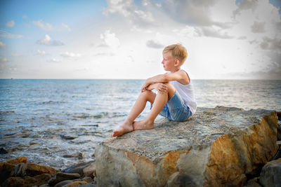 Boy on rock in sea against sky