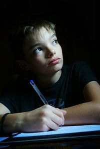 Close-up of thoughtful boy looking away while doing homework at home