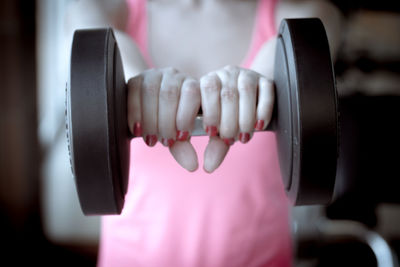 Midsection of woman lifting dumbbell in gym