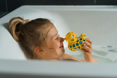 Portrait of a smiling young girl in bath with a rubber duck.