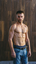 Shirtless man standing against wall