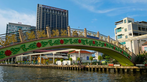 Arch bridge over river amidst buildings in city against sky