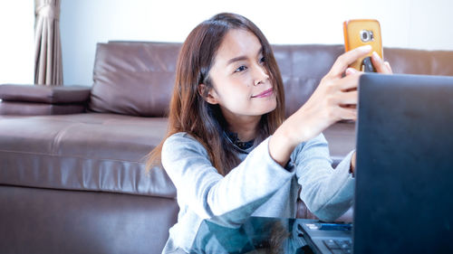 Portrait of woman using phone while sitting on sofa at home