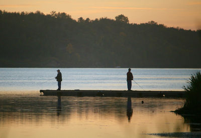 Silhouette man fishing in lake against sky during sunset