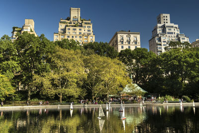 Trees by lake against buildings in city