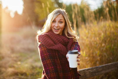 Young woman holding coffee cup while standing on field