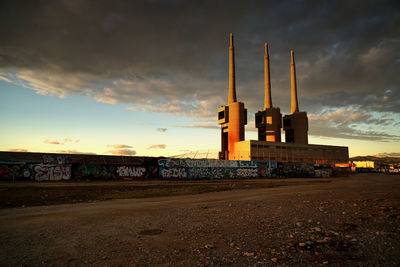 Factory on field against cloudy sky during sunset