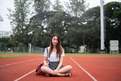 Portrait of young woman smiling while sitting on running track