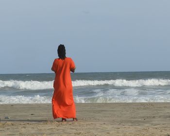 Rear view of man standing on beach against clear sky