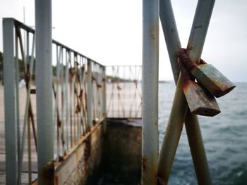 Close-up of rusty railing by bridge against sky