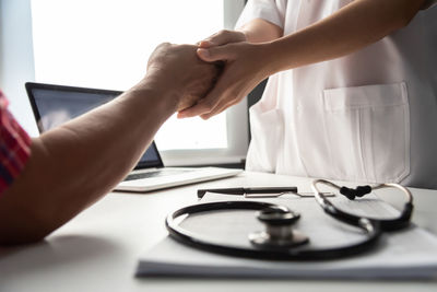 Midsection of doctor handshaking with patient in clinic