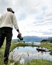 Rear view of man standing by lake against sky