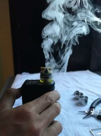 Close-up of hand holding bottle with emitting smoke on table