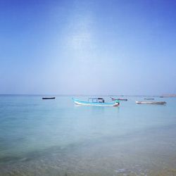 Boats moored on sea against clear blue sky