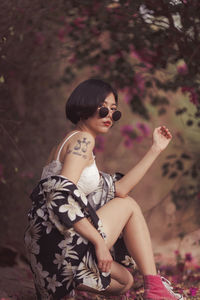 Portrait of young woman wearing sunglasses while crouching in forest