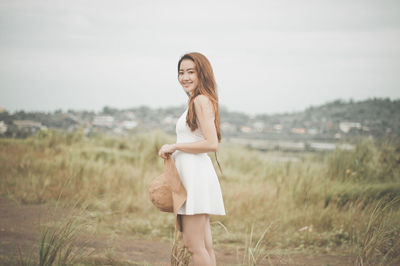 Portrait of smiling young woman standing on grass against sky