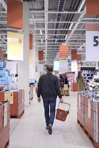 Rear view of man carrying basket while walking in supermarket