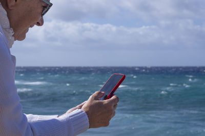 Midsection of woman using mobile phone against sea
