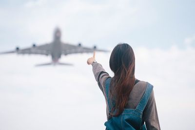 Woman pointing at airplane against clear sky