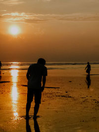 Rear view of silhouette man standing on beach against sky during sunset