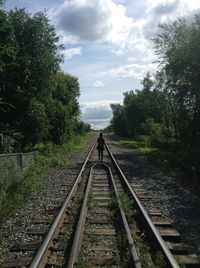 Rear view of woman walking amidst railroad tracks against cloudy sky