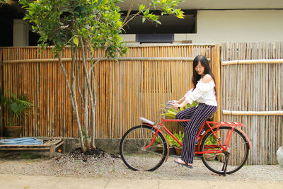 Woman sitting on bicycle against bamboo fence