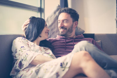 Smiling couple looking each other face to face while sitting on sofa at home