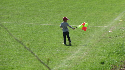 Rear view of boy waving flag at soccer field on sunny day