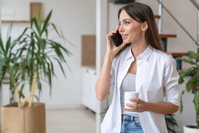 Woman talking over phone while holding coffee cup