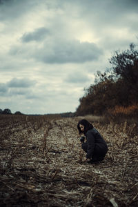 Woman with camera crouching on field against sky
