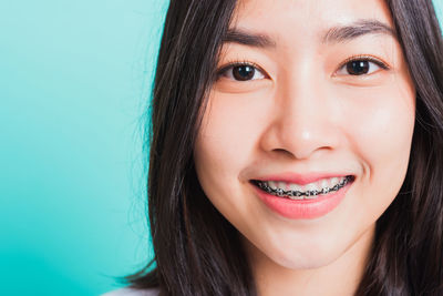 Close-up portrait of smiling young woman against blue background