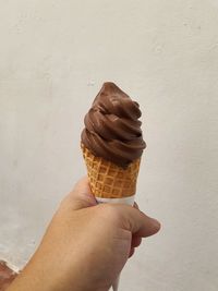 Hand holding ice cream cone against white wall