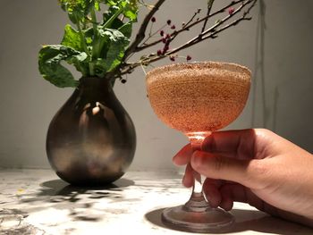 Cropped hand holding drink by plant on table