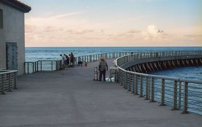 People on pier over sea against sky at sunset