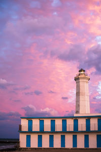 Low angle view of lighthouse by building against sky during sunset