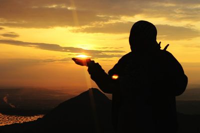 Optical illusion of silhouette man holding sun against sky during sunset