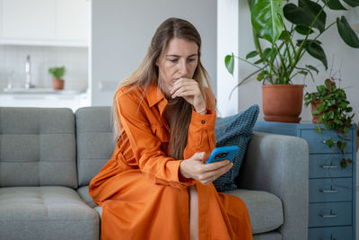 Young woman using mobile phone while sitting on sofa at home