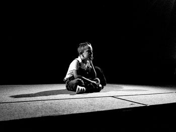 Boy sitting on floor against black background