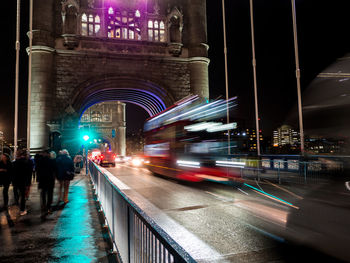 Illuminated light trails on road amidst buildings in city at night