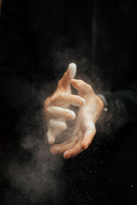 Midsection of athlete dusting chalk against black background