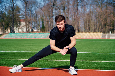 Man in sport clothers does a warm-up exercises at stadium track before jogging outdoors